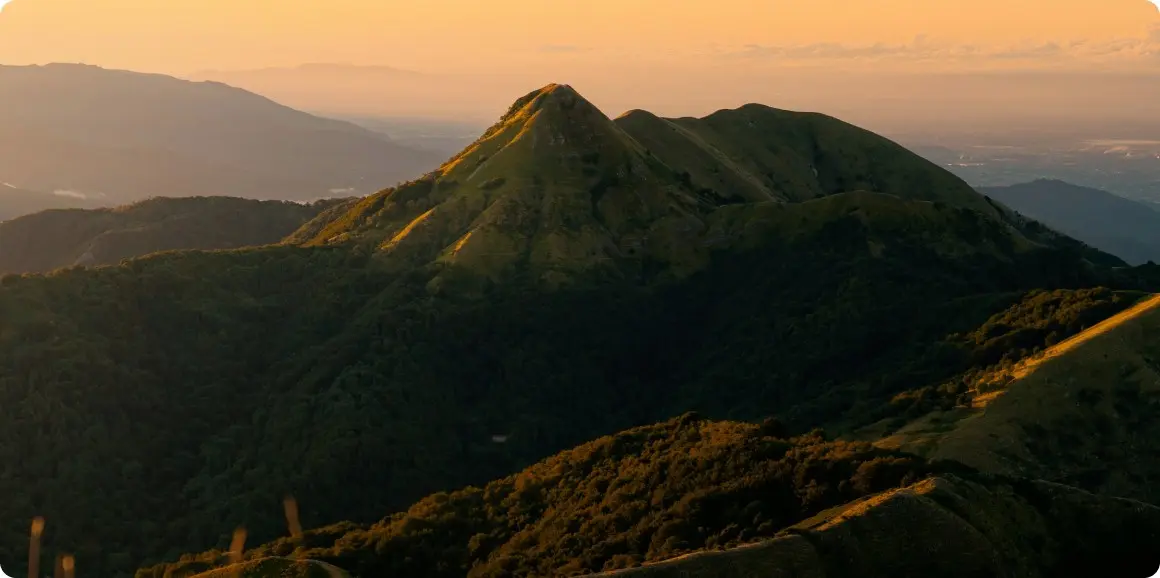 Mountain peak during sunset with lush green landscape and warm orange sky.